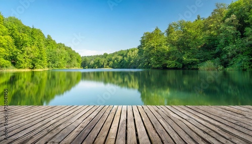 empty wooden deck with a blurred background of a peaceful lake and lush green forest under a clear sky