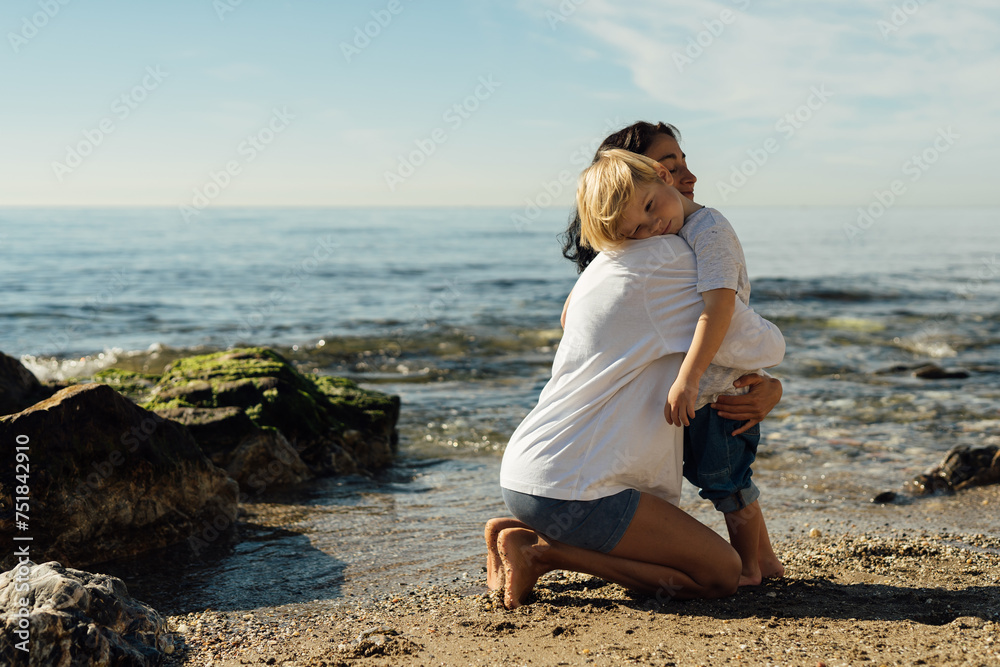 A happy mother holds her smiling son in her arms by the sea, enjoying the sea.cheerful mother and son. walk along the seashore mother and son . hugging mother and son