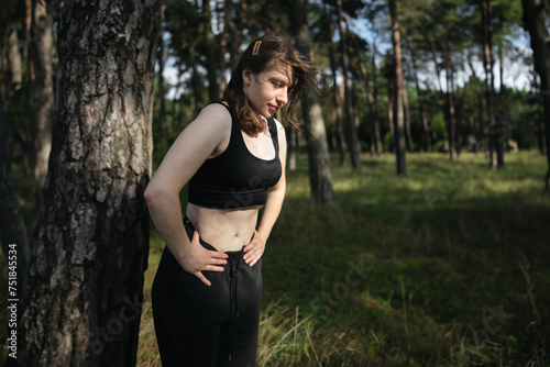 A young woman vacuums her belly outdoors in a pine forest. Nature, trees, health, body care, meditation, yoga.