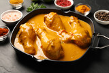 Tasty chicken curry and ingredients on black textured table, closeup