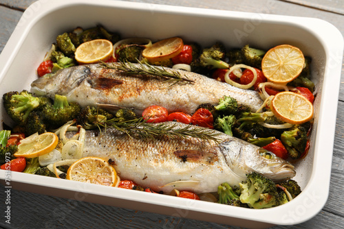 Delicious fish with vegetables and lemon in baking dish on table