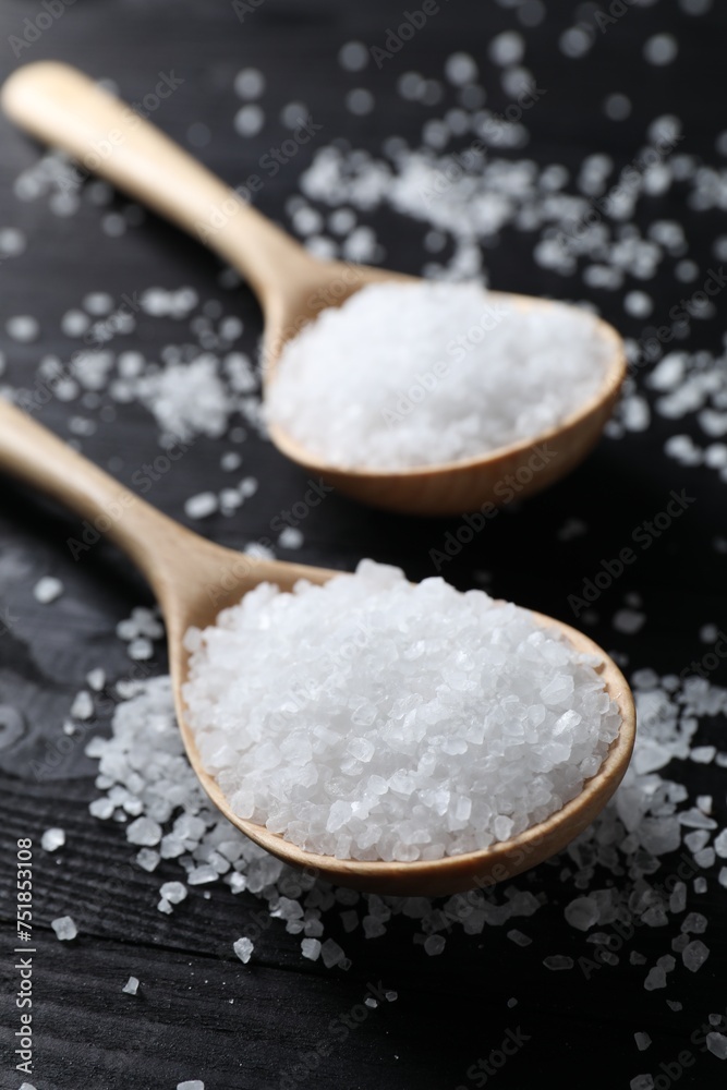 Organic salt in spoons on black wooden table, closeup Organic salt in spoons on black wooden table, closeup