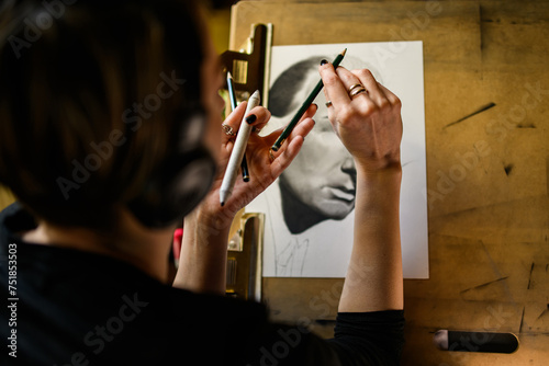 Close up of artist's hands holding a pencil and drawing a portrait.