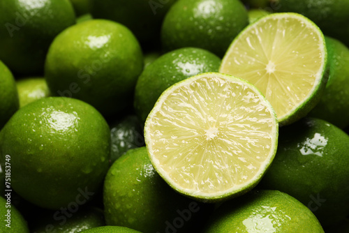 Whole and cut fresh limes with water drops as background, closeup