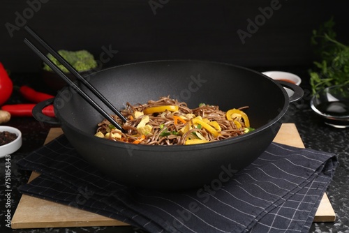 Stir-fry. Tasty noodles with vegetables, meat and chopsticks in wok on dark textured table