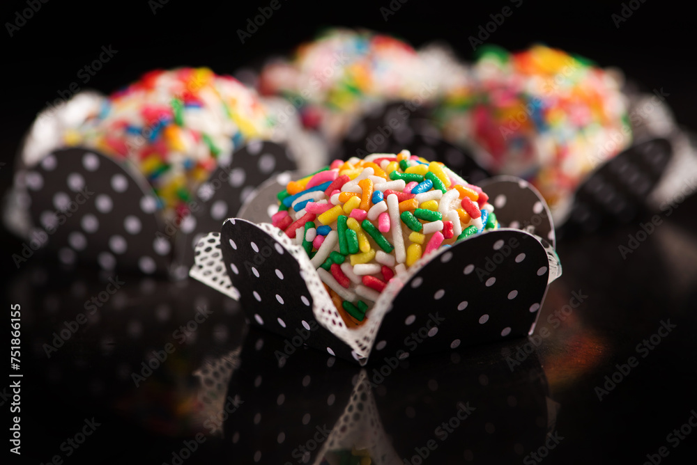 Brigadeiros, beautiful colorful sweets on black reflective surface, selective focus.