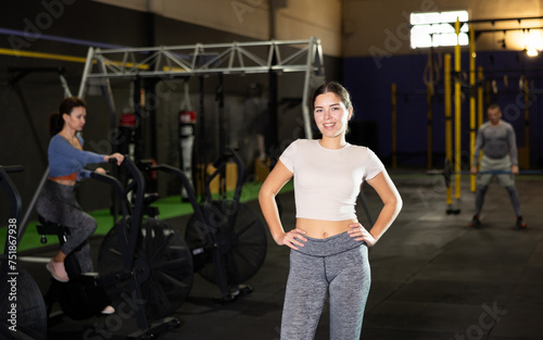 Confident smiling athletic young girl posing akimbo during break in workout in modern gym