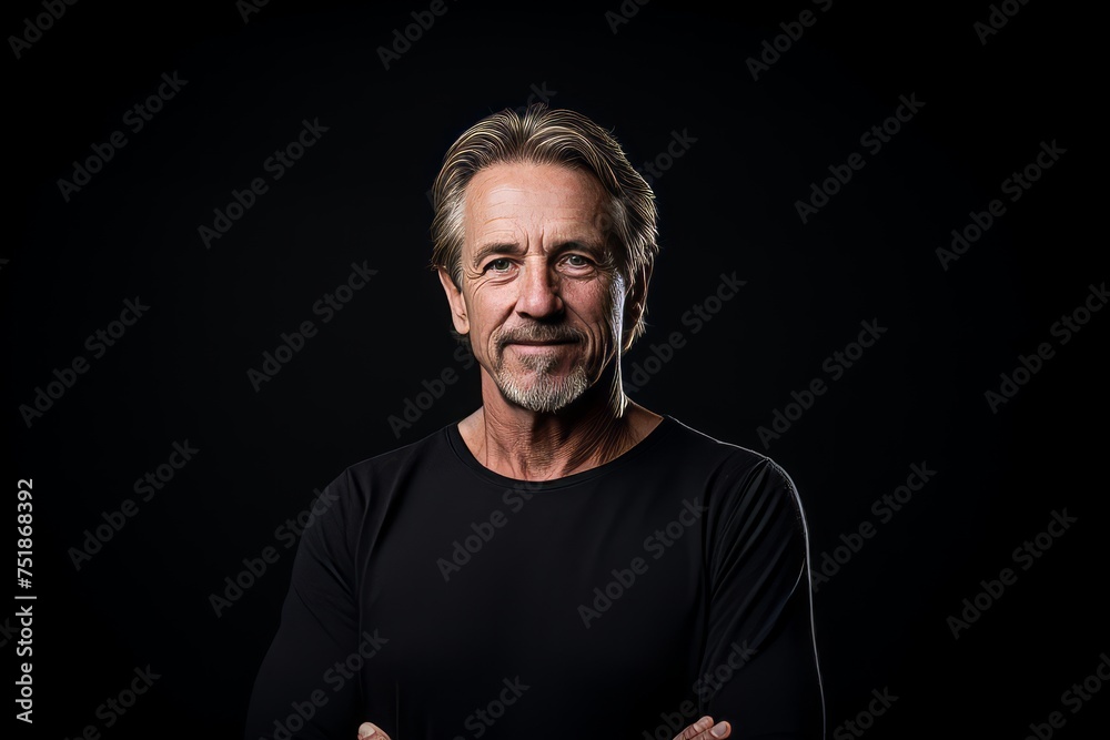 Portrait of a handsome senior man with gray hair and beard in a black t-shirt on a black background.