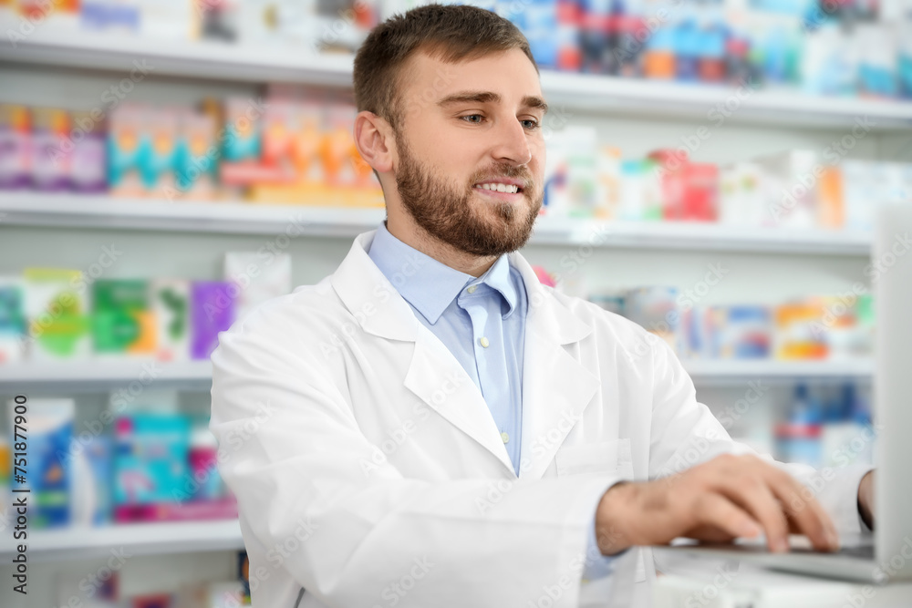 Professional pharmacist working on laptop in modern drugstore