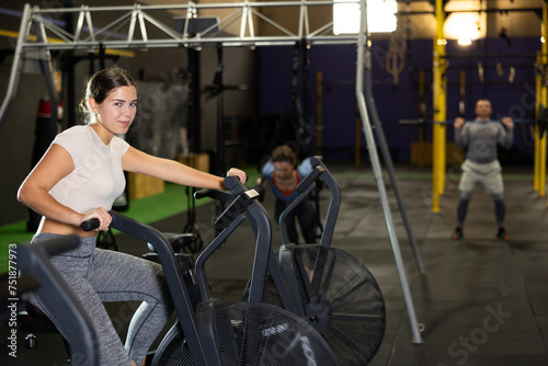Young athletic woman in sportswear training on exercise bike in gym