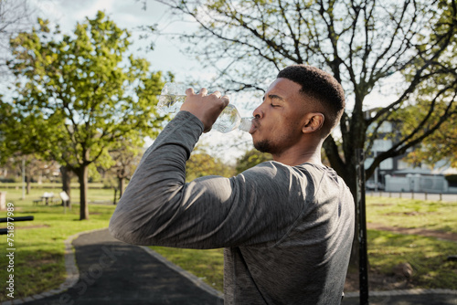 Young black man in sports clothing with closed eyes drinking water from bottle in park