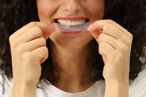 Young woman applying whitening strip on her teeth, closeup