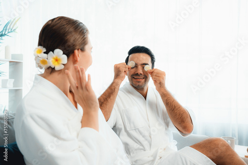Blissful couple in bathrobe playing with cucumber and enjoying daylight ambiance spa salon resort or hotel during holiday. Pampering face spa and skincare treatment with essence relaxation. Quiescent