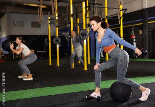 Woman during grueling workout with dumb-bell in sports hall of fitness club. Intense exercise, increased endurance. Group and personal training, development of individual couching programs