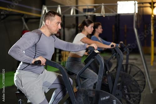 Adult athletic man in sportswear training on exercise bike in gym