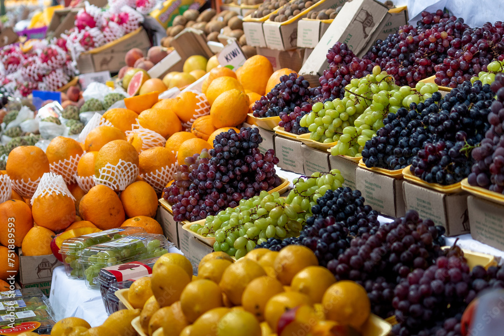 A colorful array of fresh fruits including grapes, oranges, and kiwis fills the frame at a bustling fruit market. The variety showcases nature's palette and promises freshness and taste to consumers.