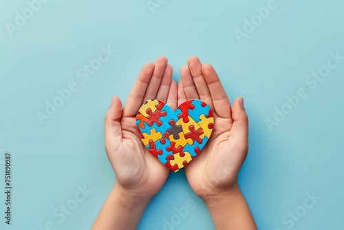 Heart made of colorful puzzle pieces on woman's hands isolated on light blue background with space for text or inscriptions, top view
