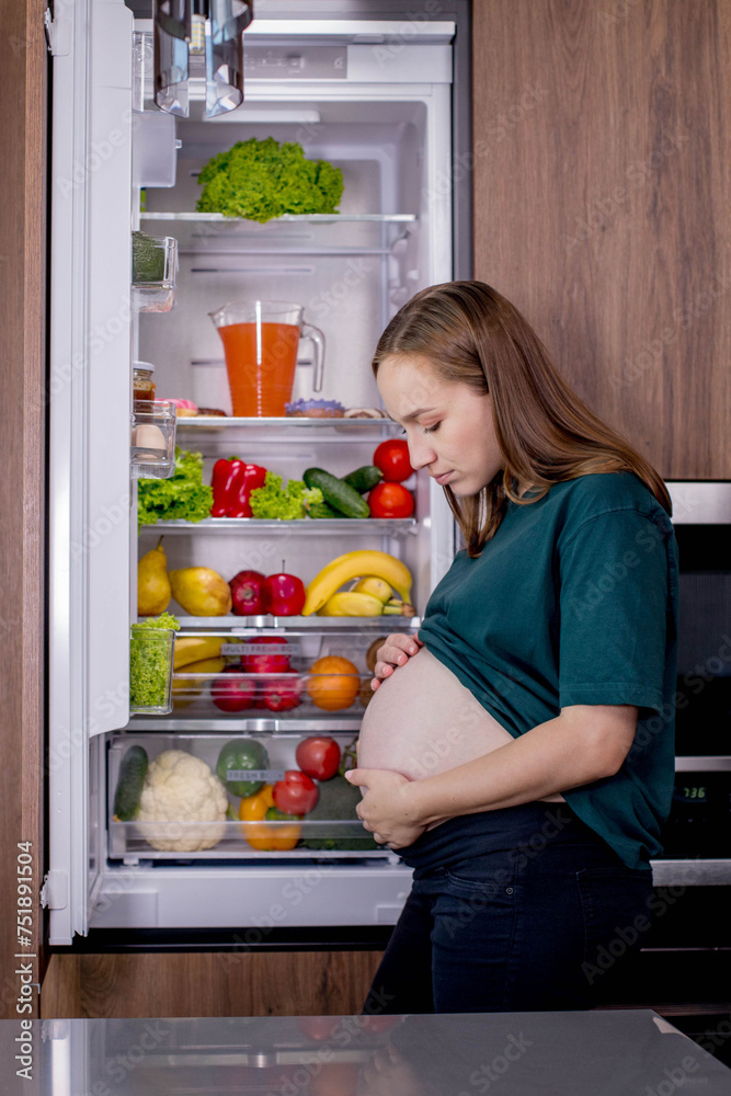 Hungry pregnant woman standing near refrigerator looking for food during pregnancy. Healthy eating