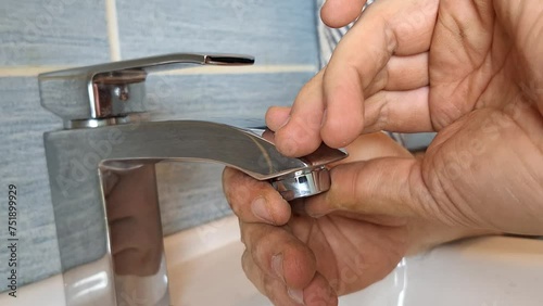 A plumber installs an aerator on a faucet. A plumber's hands fix the tap aerator to the tap. Concept of small household repairs, housekeeping, DIY, maintenance, crafts, construction photo