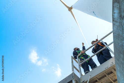 uprisen angle engineers working in fieldwork at outdoor with wind turbine and clear sky. Workers check construction. Wind turbines for electrical clean energy and environment sustainability.