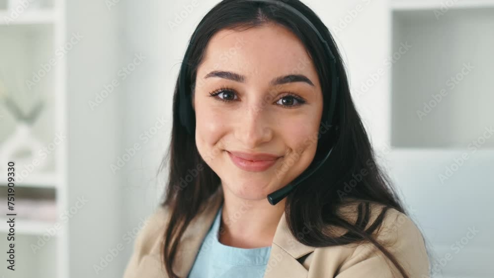 Customer support service. Close-up of arabian or indian pretty woman, call center operator with headset, working on support hotline in a modern office with a laptop, looking at camera, smiles friendly Customer support service. Close-up of arabian or indian pretty woman, call center operator with headset, working on support hotline in a modern office with a laptop, looking at camera, smiles friendly
