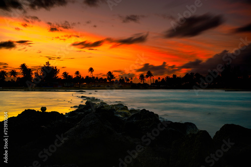 San Juan Puerto Rico Skyline at Stormy Sunset with dramatic clouds, orange sky, Palm trees, and sea waves over the volcanic rocks on La Poza del Escambrón Beach and Escambron Beach photo
