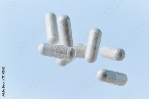 Pharmaceutical clear capsules filled with white probiotics powder closeup on light blue background dropped and spilled with petri dish 