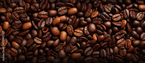 A stack of coffee beans is prominently displayed, showcasing the rich brown hues and varying sizes of the beans. The beans are clustered together, creating a textured and aromatic scene. photo