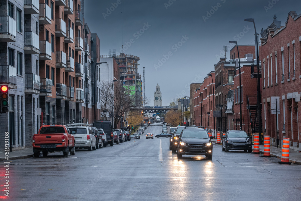 Selective blur on cars driving at dusk in Saint henri district of Montreal residential North American street with typical red brick buildings cars driving & cars parked. Atwater Market Tower is visibl