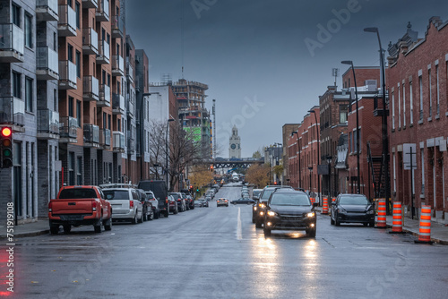 Selective blur on cars driving at dusk in Saint henri district of Montreal residential North American street with typical red brick buildings cars driving   cars parked. Atwater Market Tower is visibl