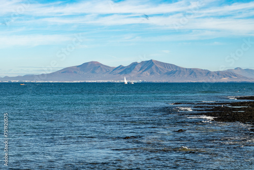 Walking on sea promenade in Corralejo along white popcorn beach with white corals, black rocks, blue water, Fuerteventura, Canary islands, Spain