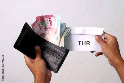 Hand holding a THR envelope filled with Indonesian Rupiah banknotes. THR or Tunjangan Hari Raya is a holiday allowance or bonus traditionally given to employees and those in need near during Ramadan photo