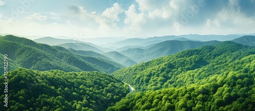 A bright summer day captures a stunning aerial view of a green mountain range. The lush, dense woods cover the rolling hills, creating a picturesque landscape.