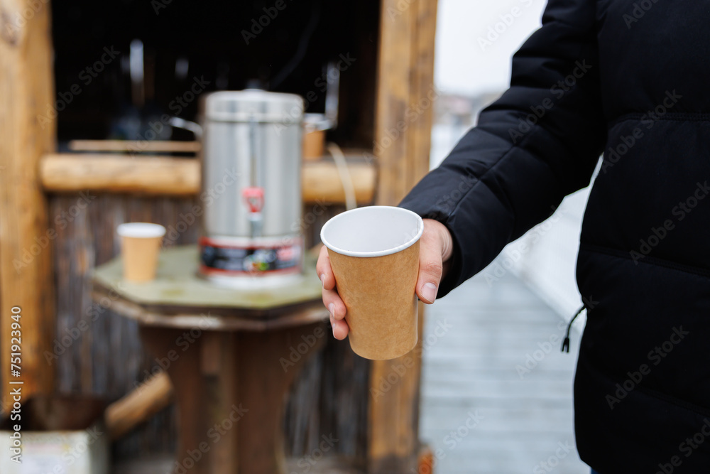 Disposable paper glass of hot tea in hand, warming in winter. Background with selective focus and copy space