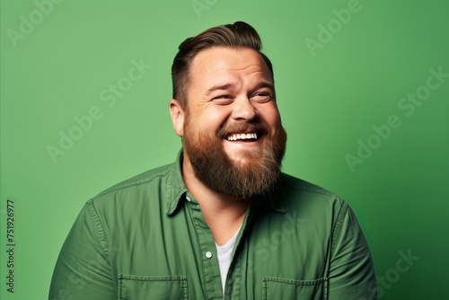 Portrait of a funny bearded man laughing against a green background.