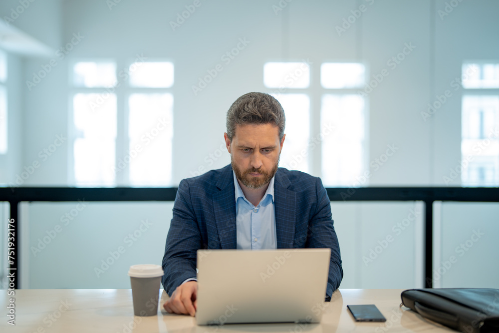 Man with laptop at office. Business man in suit in office work on laptop computer. Office worker using laptop. Business man work on laptop. Businessman have online work in modern office interior.