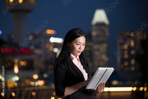 Asian businesswoman using tablet PC in city at night.