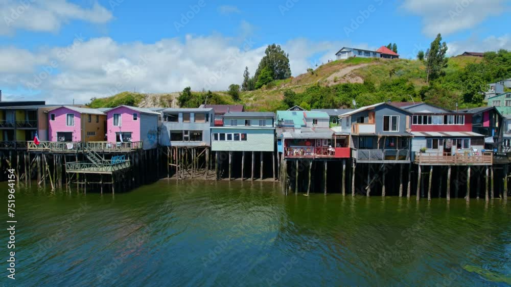 Aerial establishing shot at stilt colorful houses of Castro Chiloé Patagonian island sea bay landscape with high tide, blue water, green south American hills, travel destination Aerial establishing shot at stilt colorful houses of Castro Chiloé Patagonian island sea bay landscape with high tide, blue water, green south American hills, travel destination