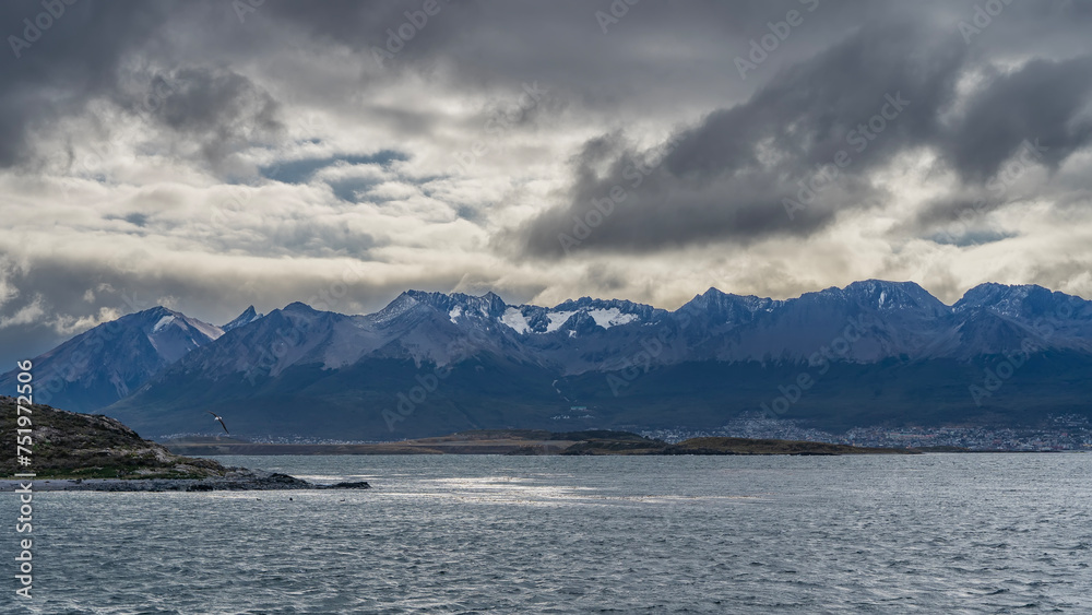 A beautiful snow-capped mountain range of the Andes against a cloudy sky. View from the Beagle Canal. Ripples on the blue water. Argentina. Tierra del Fuego Archipelago.