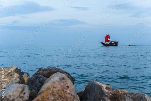 A ship with red sails sails on the sea after sunset