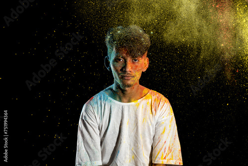Asian man splashed with colorful holi powder and having fun isolated on black background. © Leo Lintang