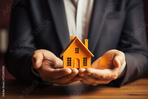 A businessman in a suit holds a model of a house on his palms. Male hands holding house model .