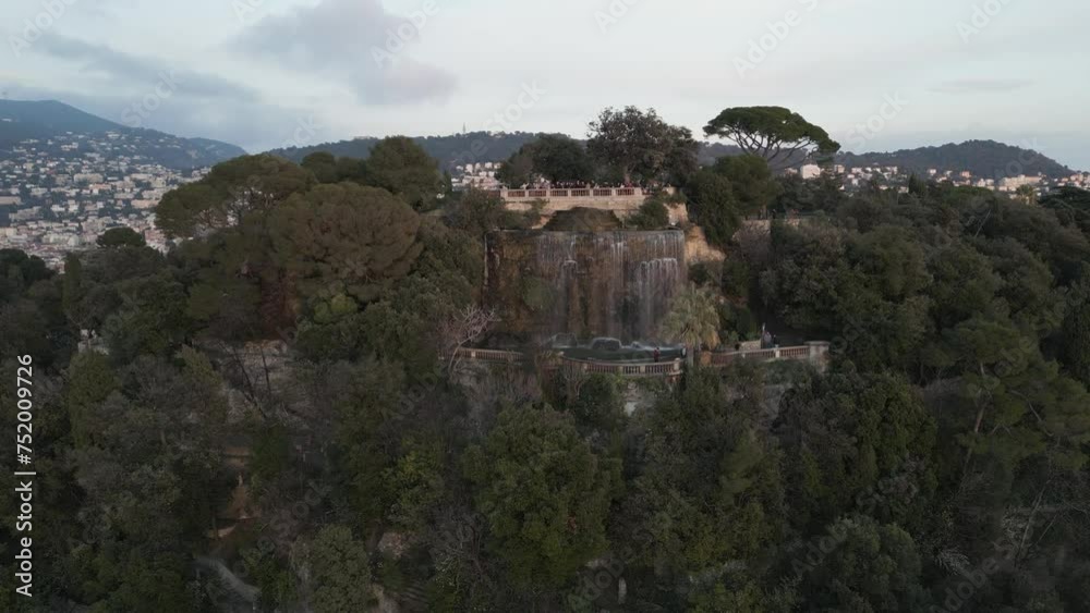 Waterfall on Top of a Hill in French Riviera Next to Vegetation and City of Nice, Mediterranean Sea. Tourists Above Taking Pictures of Sunset. Drone View Waterfall on Top of a Hill in French Riviera Next to Vegetation and City of Nice, Mediterranean Sea. Tourists Above Taking Pictures of Sunset. Drone View