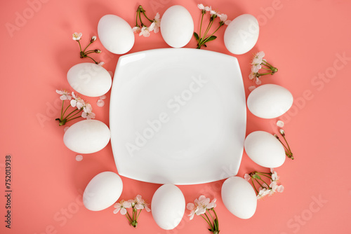 Composition with an empty plate, Easter eggs and beautiful flowers on a pink background, close-up. Space for copying. View from above.