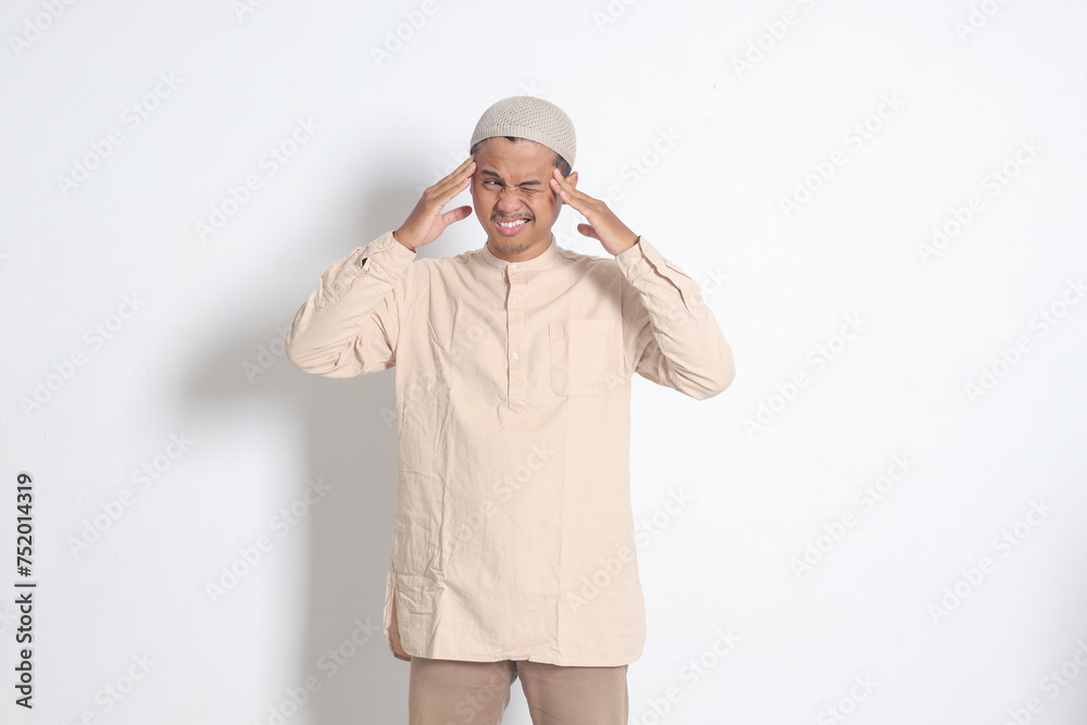 Portrait of suffering Asian muslim man in white shirt having a migraine, touching his temple. Headache disease concept. Isolated image on white background Portrait of suffering Asian muslim man in white shirt having a migraine, touching his temple. Headache disease concept. Isolated image on white background
