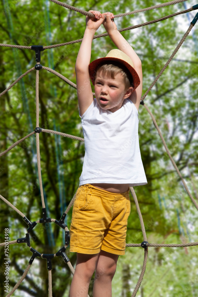 A child climbs up an alpine grid in a park on a playground on a hot summer day