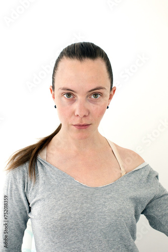 Young adult woman with a ponytail and combed hair looks at the camera photo at documents in a gray sweater with an open shoulder on a white background