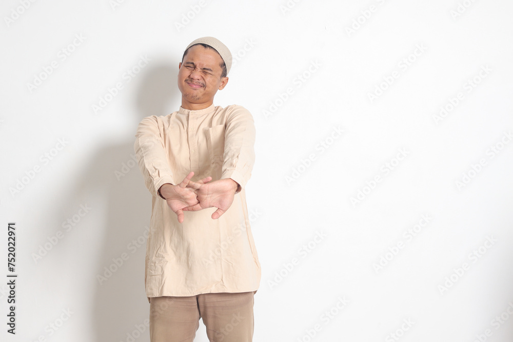 Portrait of overworked Asian muslim man in koko shirt with skullcap stretching his hands and body after waking up. Sleep deprivation concept. Isolated image on white background Portrait of overworked Asian muslim man in koko shirt with skullcap stretching his hands and body after waking up. Sleep deprivation concept. Isolated image on white background