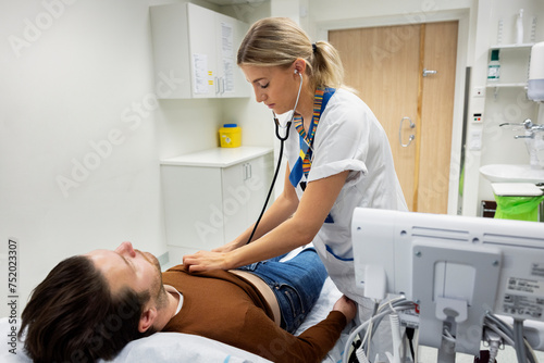 Female doctor checking patient with stethoscope lying on bed in examination room