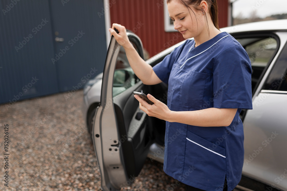 Female healthcare worker using mobile phone by car standing in back yard Female healthcare worker using mobile phone by car standing in back yard